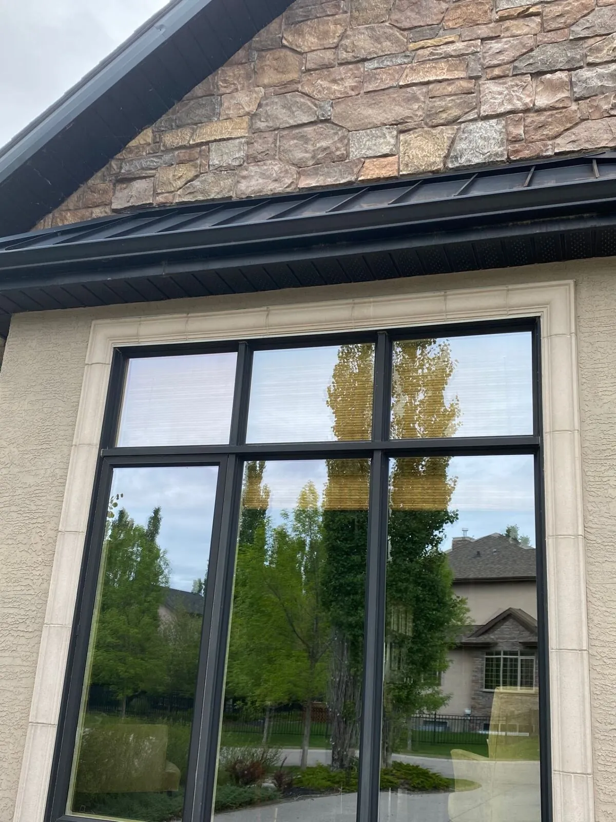 Black-frame picture window on a stucco and stone home